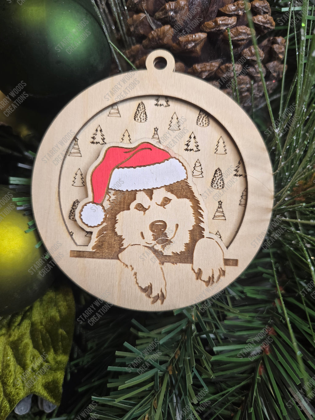 Wooden Christmas ornament with an alaskan malmute wearing a Santa hat, layered on top of a festive pattern, on a green pine branch.
