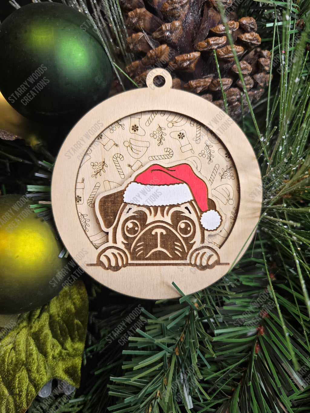 Wooden Christmas ornament with a pug wearing a Santa hat, layered on a festive background piece, on a tree.