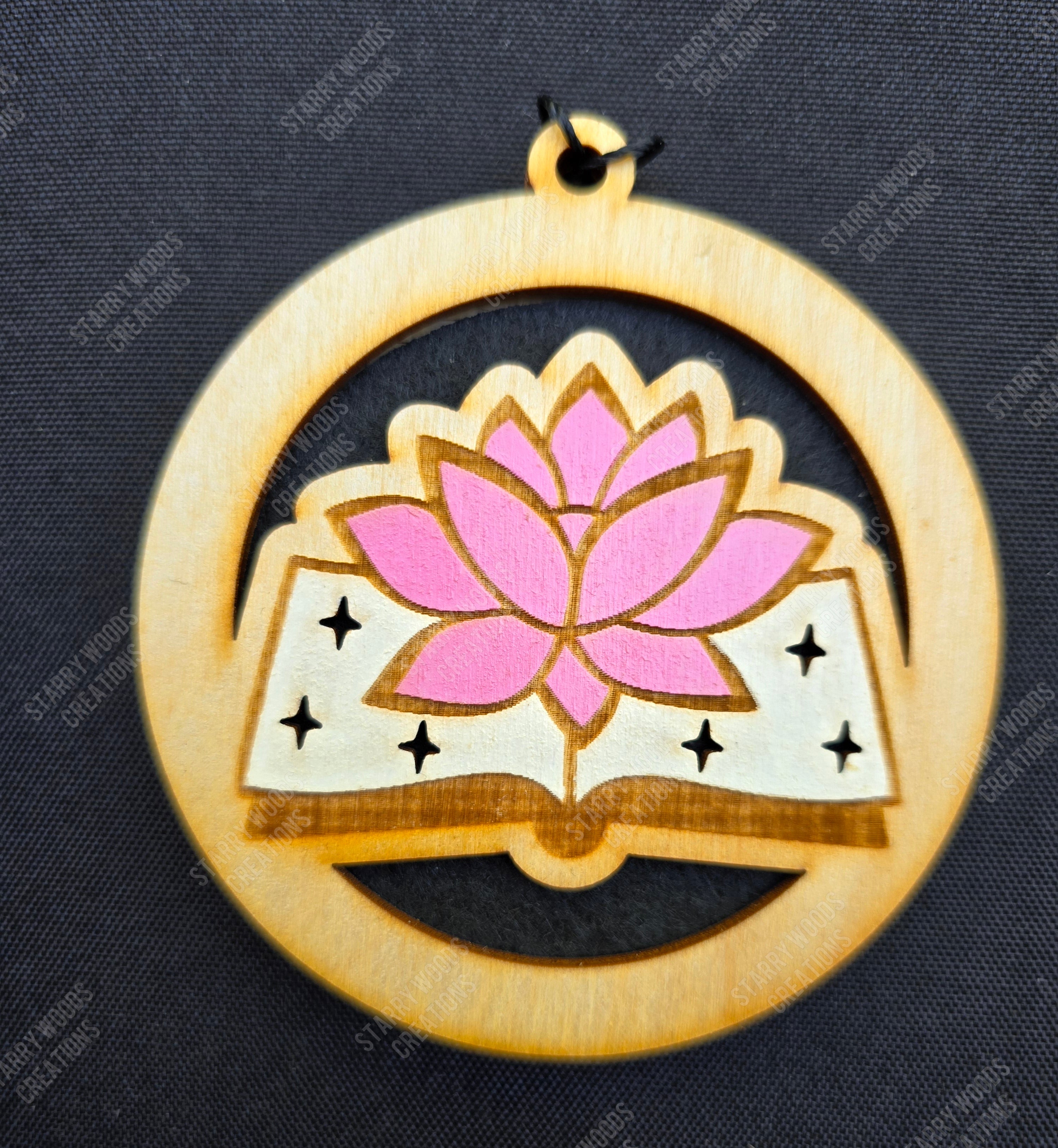 Decorative wooden hanging air freshener with pink lotus flower in an open book design on a black background
